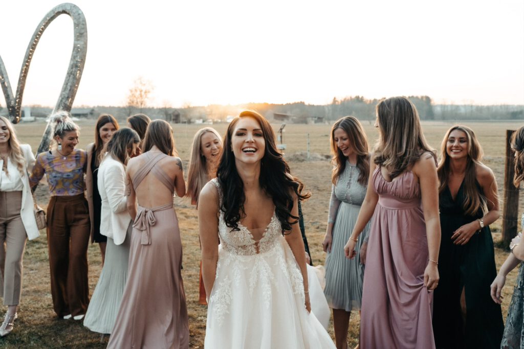 Die Braut lacht glücklich, umgeben von ihren Freundinnen in stilvollen Kleidern, während die Abendsonne die Hochzeit in warmes Licht taucht.